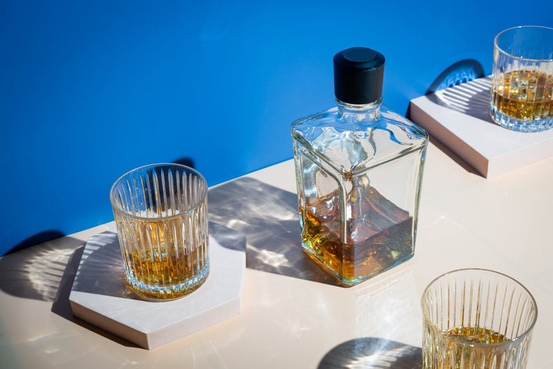 A bottle of alcohol with three half-filled glasses of alcohol on a table. 