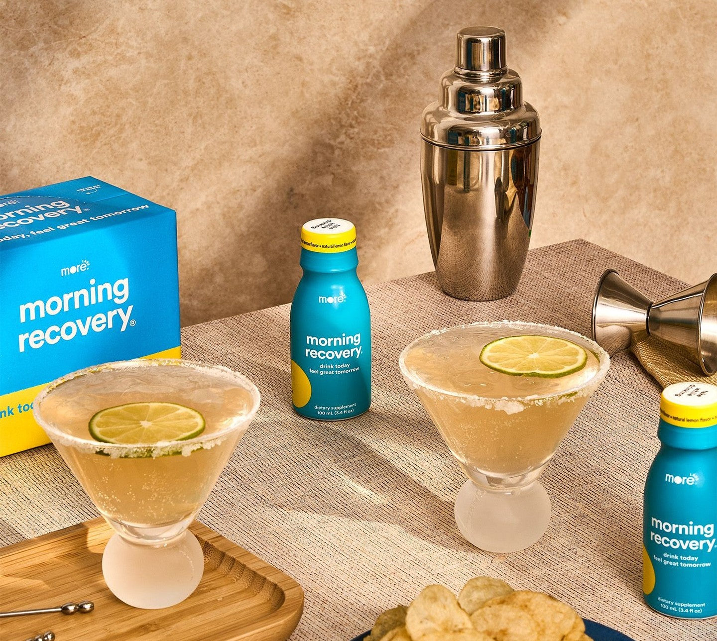 Two bottles of Morning Recovery supplement are placed on a glass table with two wine glasses. 
