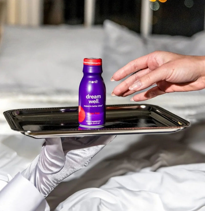 More Labs Dream Well bottle placed on a tray over a bed with a relaxing nighttime setting.