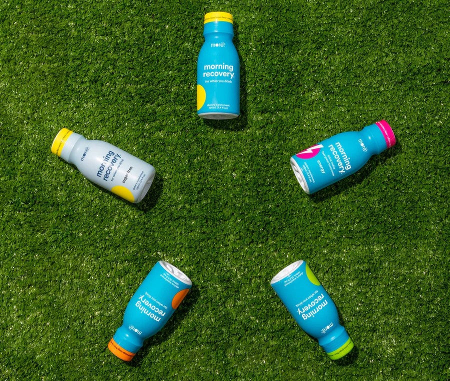 Five small, colorful bottles from More Labs, arranged in a star shape on a green, grass-like surface.