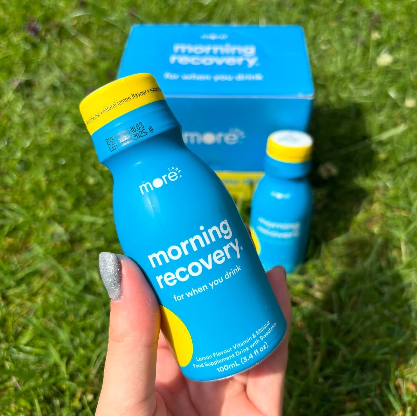 More Labs Morning Recovery bottle with a product box and another bottle placed on green grass in the background.