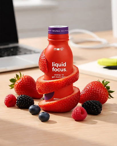 More Labs Liquid Focus bottle with berries on a desk beside a laptop.