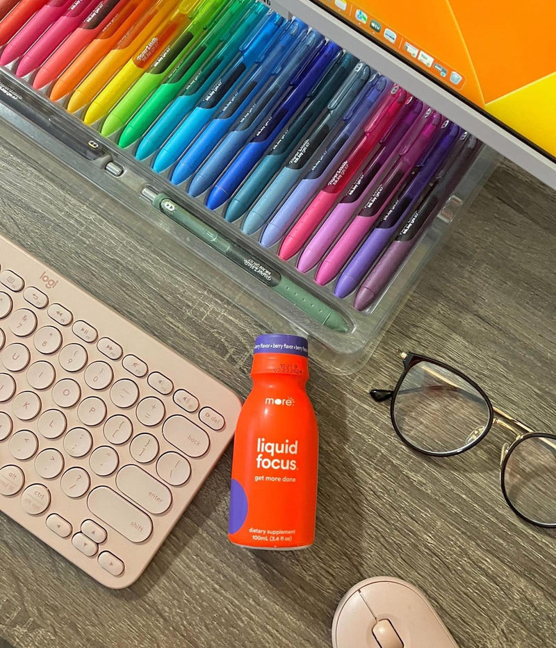 More Labs Liquid Focus bottle on a desk with a keyboard, glasses, and colorful pens.