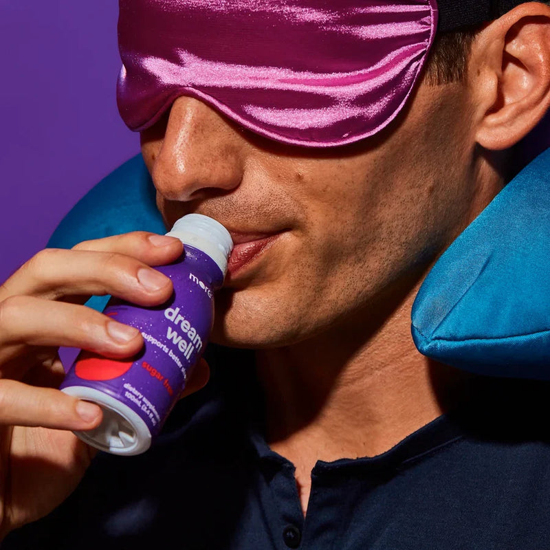Man wearing a sleep mask and travel pillow drinks More Labs Dream Well.