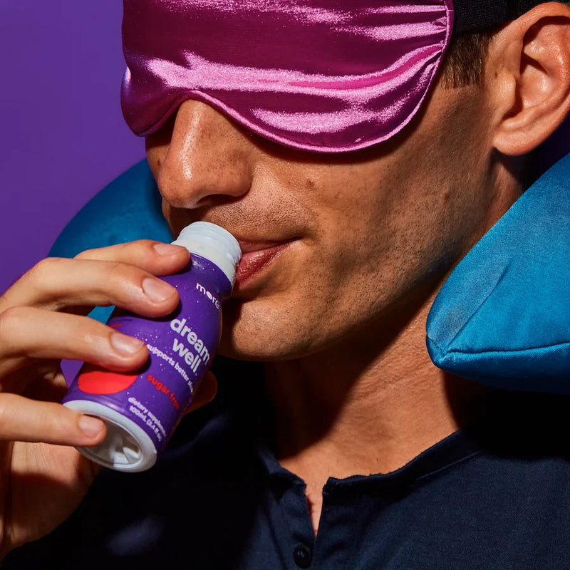 More Labs Dream Well bottle held by a man wearing a satin sleep mask and travel pillow.