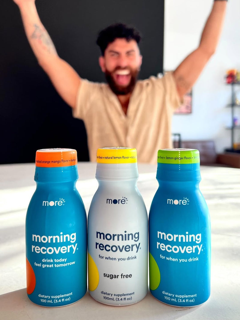 Three Morning Recovery dietary supplement bottles by More Labs on a table with a cheering man in the background.