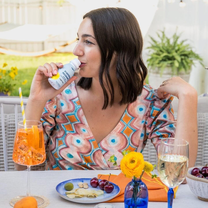 Woman enjoying a More Labs’ Sugar-Free Morning Recovery dietary supplement at an outdoor brunch table.