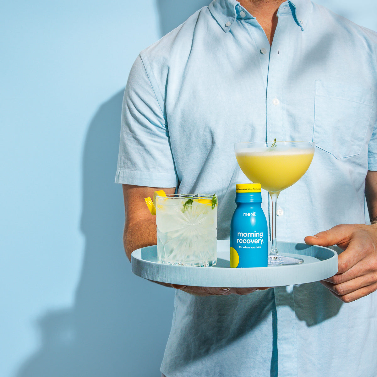 Person holding a tray with cocktails and a More Labs Morning Recovery drink bottle.
