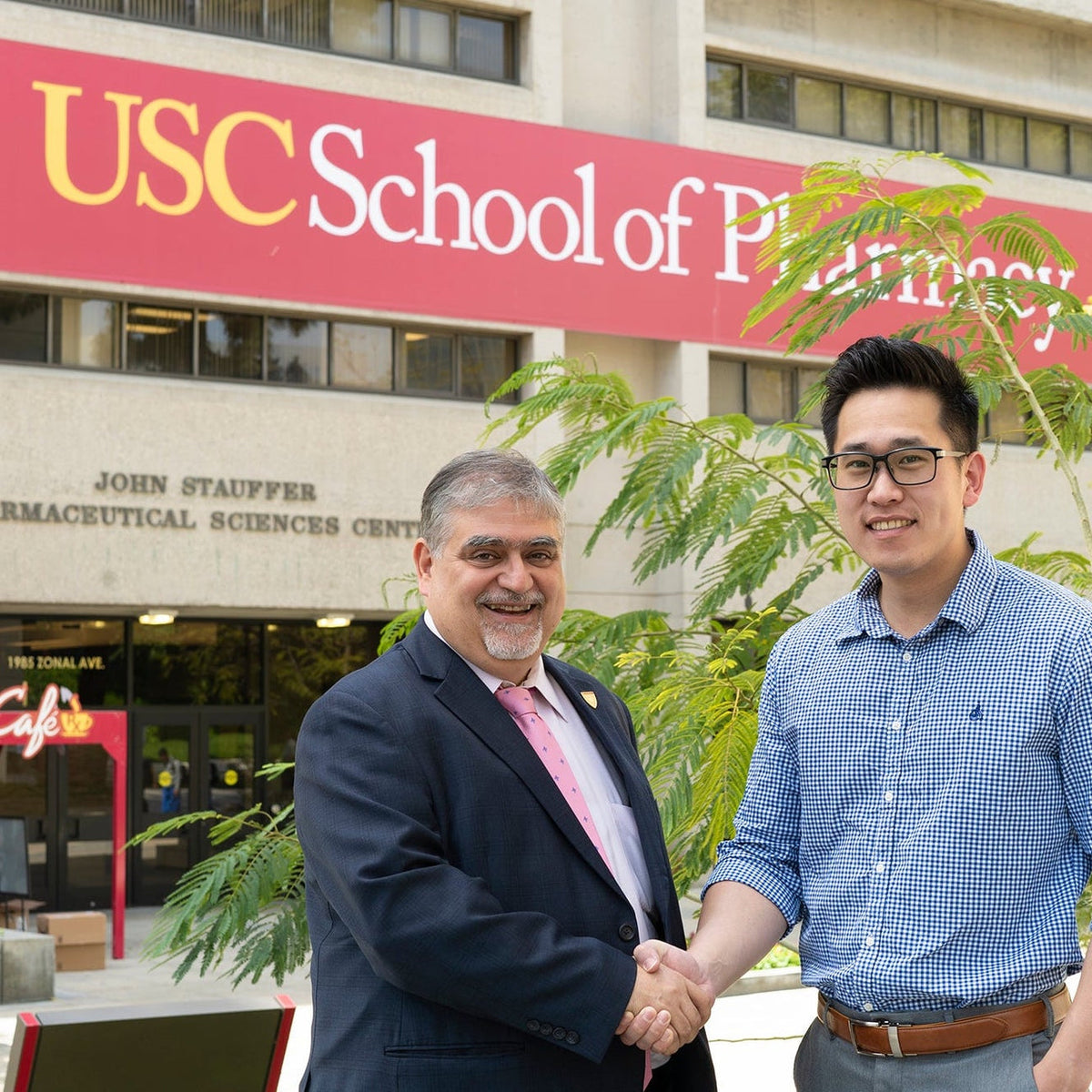 Two professionals shaking hands in front of the USC School of Pharmacy building, representing the USC x More Labs partnership collaboration.
