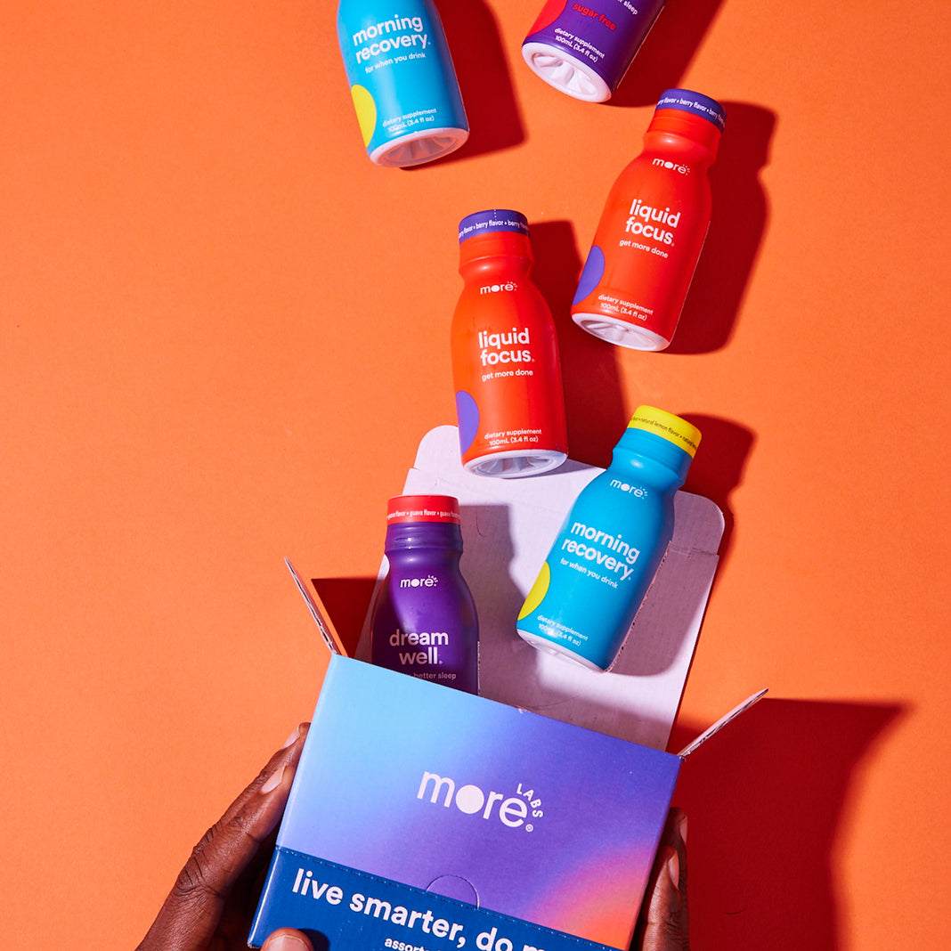 Assorted More Labs wellness shot bottles, including Morning Recovery, Liquid Focus, and Dream Well, floating above an open branded box on an orange background.
